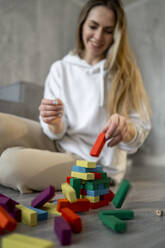 Lächelnde Frau, die zu Hause mit mehrfarbigen Spielzeugblöcken spielt - ANAF00796