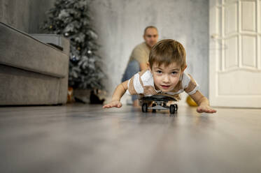 Vater mit Sohn spielt zu Hause auf dem Skateboard - ANAF00813