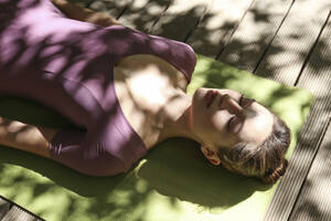 Frau mit geschlossenen Augen auf einer Übungsmatte im Sonnenlicht liegend - SYEF00214