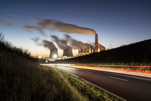 UK, England, Nottingham, Light trails stretching along asphalt road at dusk with coal-fired power station in background - WPEF06859