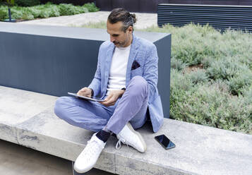 Mature man using tablet PC sitting on bench - RFTF00343