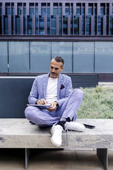 Mature businessman using tablet PC sitting with legs crossed at ankle on bench - RFTF00345