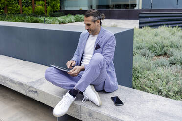 Mature businessman using tablet PC sitting on bench - RFTF00346