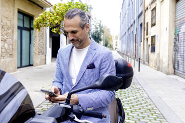 Mature businessman using mobile phone sitting on motorcycle - RFTF00360