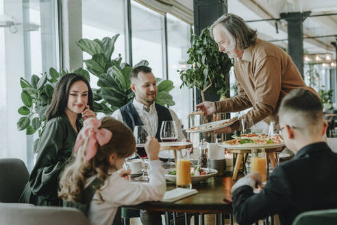 Älterer Mann serviert seiner Familie im Café das Essen - YTF00495