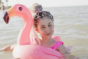 Lächelndes Mädchen mit Spaß auf rosa Flamingo aufblasbaren Ring im Meer - OSF01302