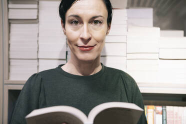 Smiling woman with book in front of bookshelf - AMWF01077