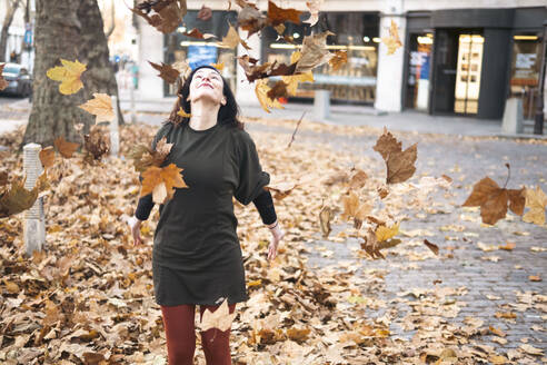 Frau spielt mit Herbstblättern auf dem Fußweg - AMWF01078