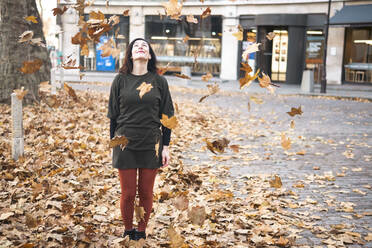 Frau steht inmitten fallender Herbstblätter auf dem Fußweg - AMWF01079