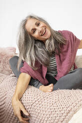 Happy mature woman with gray hair sitting on sofa - JBYF00222