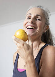 Happy mature woman eating apple at home - JBYF00231