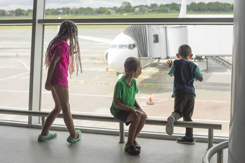 Girl with brothers watching preparation of airplane for boarding from airport terminal window - OSF01304