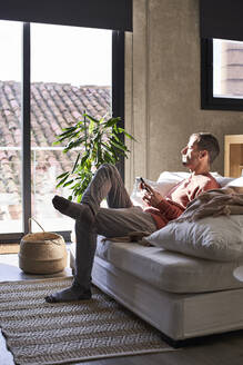 Mann mit Smartphone sitzt zu Hause auf dem Sofa - VEGF06139