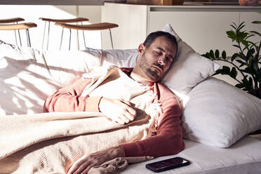 Man sleeping by smart phone on sofa at home - VEGF06147