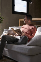 Thoughtful man sitting with book on sofa at home - VEGF06149
