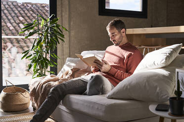 Man sitting on sofa reading book at home - VEGF06150