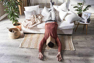 Man with book on face lying upside down at home - VEGF06157