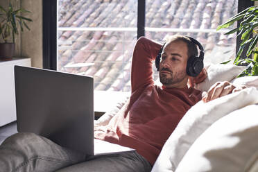 Mann mit Kopfhörern sieht sich zu Hause einen Film auf dem Laptop an - VEGF06162