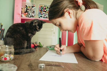 Katze beobachtet Mädchen beim Zeichnen von Bildern auf Papier zu Hause - OSF01314