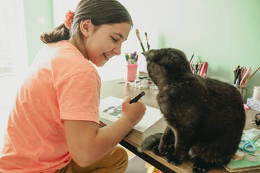 Glückliches Mädchen schaut auf eine Katze, die auf dem Tisch sitzt - OSF01315