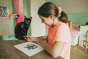 Mädchen gibt Katze, die zu Hause auf dem Tisch sitzt, einen Filzstift - OSF01316