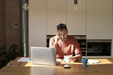 Stressed man sitting with financial bills on desk at home - VEGF06166