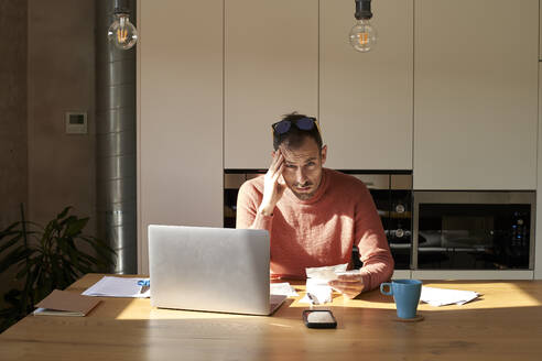 Stressed man sitting with financial bills on desk at home - VEGF06166