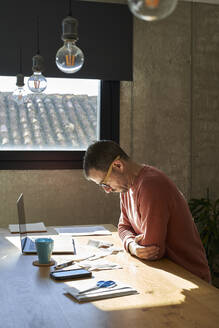 Sad man with financial bills and laptop sitting at desk - VEGF06169