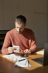 Man with financial bills calculating on smart phone at desk - VEGF06179