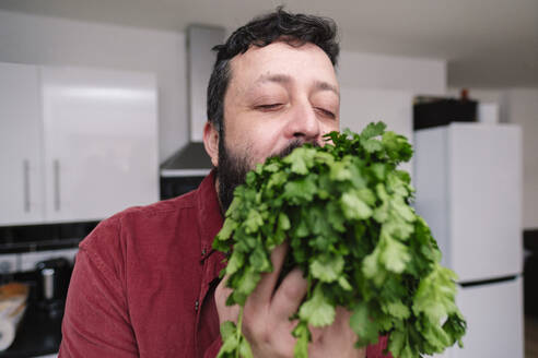 Mature man with eyes closed holding cilantro at home - ASGF03227