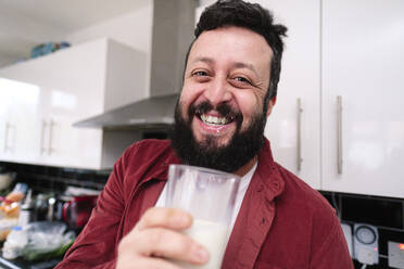 Glücklicher Mann hält ein Glas Milch in der Küche zu Hause - ASGF03233