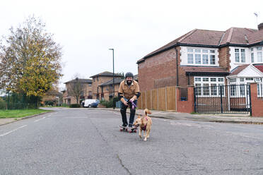 Mature man learning skateboarding with pet on road - ASGF03240