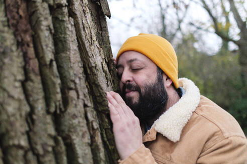 Mann mit geschlossenen Augen lehnt an einem Baum im Wald - ASGF03249