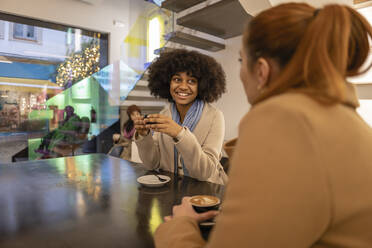 Glückliche Frau hält eine Kaffeetasse und spricht mit einem Freund in einem Café - JCCMF08680