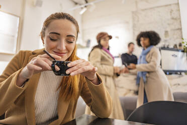 Smiling woman holding coffee cup with friends standing in background - JCCMF08686