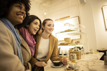 Cheerful young woman with friends standing at table in cafe - JCCMF08692