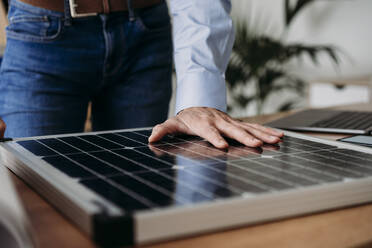 Hand eines Geschäftsmannes auf einem Solarpanel im Büro - EBBF07557