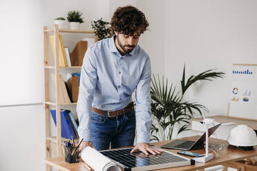 Young businessman looking at solar panel at desk in office - EBBF07558