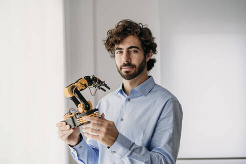 Young businessman holding robotic arm in office - EBBF07590