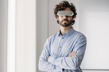 Ingenieur mit Virtual-Reality-Brille steht mit verschränkten Armen im Büro - EBBF07595