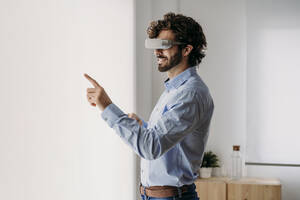 Geschäftsmann mit VR-Brille berührt transparenten Bildschirm im Büro - EBBF07599