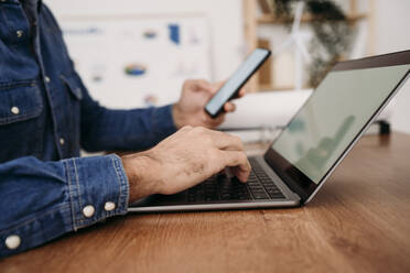 Hände eines Ingenieurs, der auf einem Laptop tippt und ein Smartphone im Büro hält - EBBF07614