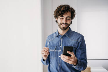 Smiling young entrepreneur using mobile phone in office - EBBF07630