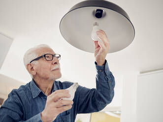 Senior man changing old lightbulb for a LED energy saving lightbulb - PWF00396