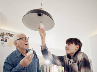 Grandson and grandfather changing old lightbulb for a LED energy saving lightbulb - PWF00397
