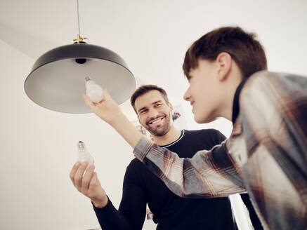 Son and father changing old lightbulb for a LED energy saving lightbulb - PWF00398