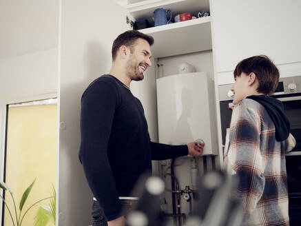 Smiling son and father checking boiler for energy saving at home - PWF00401