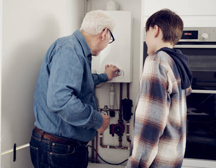 Grandson and grandfather adjusting boiler for energy saving at home - PWF00403