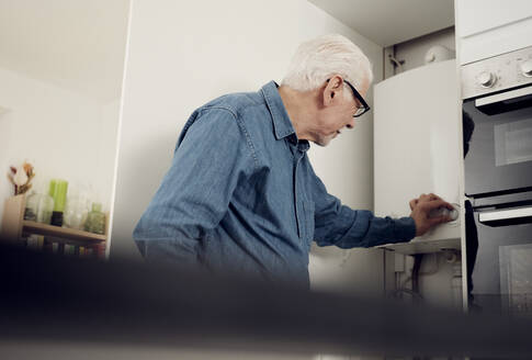 Senior man adjusting boiler for energy saving at home - PWF00405