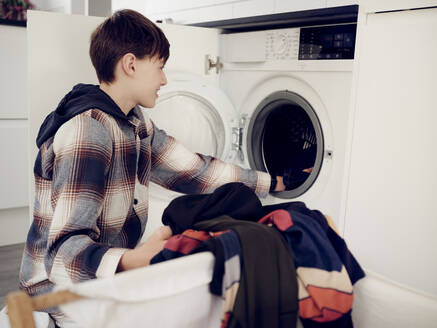Boy putting laundry into washing machine at home - PWF00406